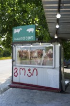 A small stand with meat presentation and signs, surrounded by green trees, butcher, small, mobile