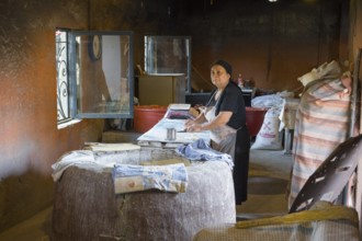 An elderly woman works in a traditional, rustic bakery with bread and baking supplies, bakery,