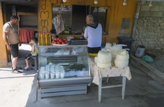 Market stall with cheese and tomatoes surrounded by a few people in an urban environment selling