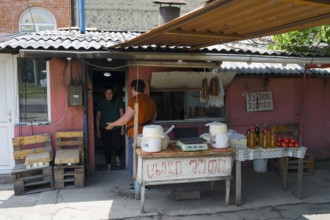 A rustic market stall with handmade products and people talking, selling cheese and tomatoes and