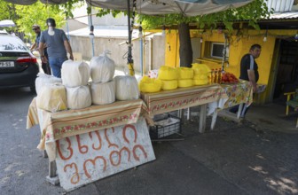 Market stand with various types of cheese and products under trees at a busy market selling cheese,