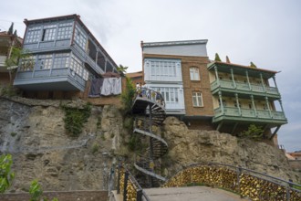 Traditional buildings with wooden balconies stand on a rock with a spiral staircase, Abanotubani
