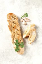 Garlic bread, baguette with garlic butter and herbs, on a light table, top view