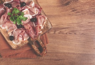 Sliced prosciutto, on a cutting board, with olives and herbs, snack, breakfast, no people