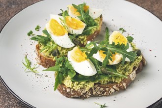 Sandwich with mashed avocado, boiled egg, and arugula, on bread, homemade, breakfast