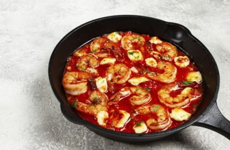 Greek saganaki, in an iron pan, saganaki with shrimp, shrimp in tomato sauce, with pepper and feta