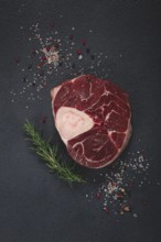 A shank on the bone, raw meat for ossobuco, on the table, with a branch of rosemary, top view, no