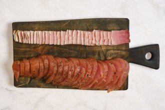A wooden cutting board displays two types of cured meat. One side has thin slices of pink meat