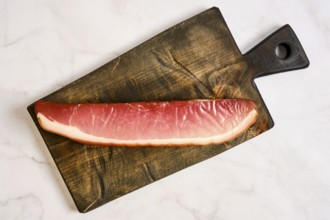 A long piece of cured parma ham on a wooden cutting board. The board has a rustic design and is