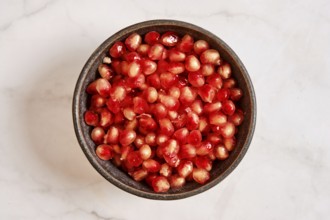 A bowl is filled with bright red pomegranate seeds. These seeds are fresh and cut from the fruit.