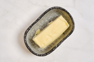 A piece of butter in a grey dish on a white countertop. This setting shows a kitchen environment