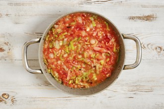 A pot filled with a mixture of chopped vegetables and tomatoes on a wooden kitchen counter. The