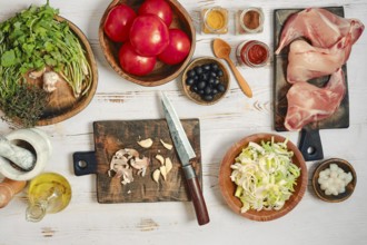 Fresh tomatoes, herbs, and spices are laid out on wooden boards in a kitchen. A knife and cutting