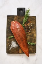 Cured turkey meat on a wooden cutting board. Around it are herbs, spices, and salt. The setting is