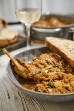 A plate features rabbit meat cooked with vegetables in sauce. Slices of bread rest next to the dish
