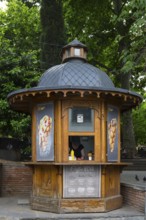 Traditional wooden kiosk with ice cream advertising surrounded by trees in an urban park, antique