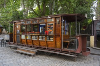 Wooden tram as a food stand with fruit in cups on a tree-lined cobblestone street, tram bar, old