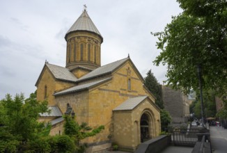 Historic church with yellow stone architecture and dome surrounded by trees on a cloudy day, Sioni