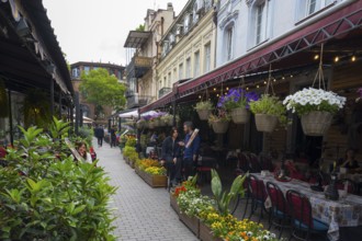 Lively street with outdoor cafés and colorful flowers along historic buildings, Old Town, Tbilisi,