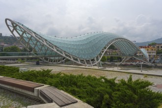 Wavy, modern glass bridge across parkland with hills in the background, Peace Bridge, Rike Park,