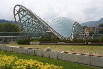Modern glass roof of a bridge in wave form with surrounding park area, Peace Bridge, Rike Park,