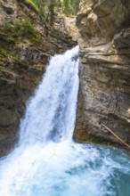 Powerful waterfall plunging into a vibrant turquoise pool in johnston canyon, creating a