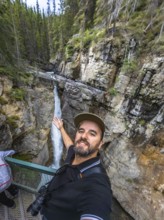 Photographer taking a selfie on a metal walkway, capturing the majestic johnston canyon waterfall