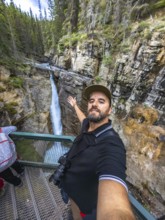 Tourist taking a selfie with outstretched arm at johnston canyon lower falls, showcasing the