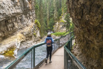 Female tourist with backpack walking on a metal catwalk enjoying the scenic view of johnston canyon