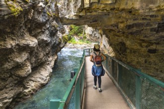 Female tourist with backpack walking on a metal catwalk built into the side of johnston canyon,
