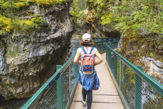 Female tourist with backpack walking on metal catwalk enjoying the view of johnston canyon and the