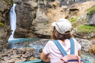 Female tourist wearing a backpack and baseball cap admiring a stunning waterfall cascading into