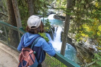 Female hiker wearing backpack and cap admiring cascading waterfalls and turquoise water of johnston