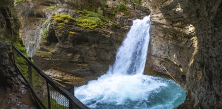 Powerful waterfall cascading into a turquoise pool in johnston canyon, surrounded by rocky cliffs