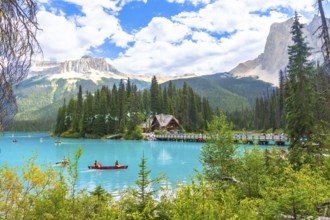 Canoeing tourists navigate the turquoise waters of emerald lake, with a wooden lodge and bridge set
