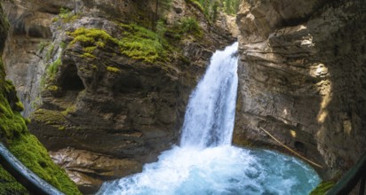 Sunlight illuminating the vibrant turquoise pool at the base of a cascading waterfall in johnston