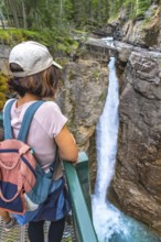 Female tourist carrying a backpack and baby carrier, enjoying the stunning view of a waterfall