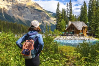 Tourist with a backpack is enjoying the breathtaking view of emerald lake and its charming wooden