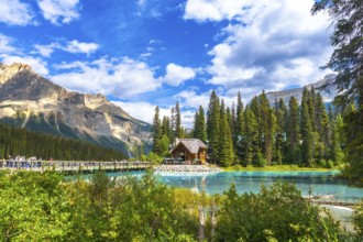 Wooden lodge reflecting on turquoise water with tourists walking on a bridge, surrounded by