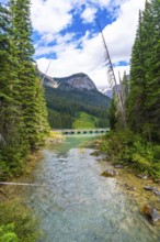 Turquoise water flows from emerald lake under a bridge and into yoho national park, framed by lush