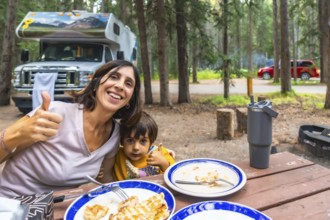 Mother and child showing thumbs up while having lunch at their campsite in banff national park,