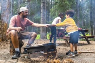 Father serving food to children at campsite, cooking on campfire in banff national park, canadian
