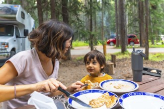Mother giving grilled food to her child while having lunch at a campsite in the canadian rockies,