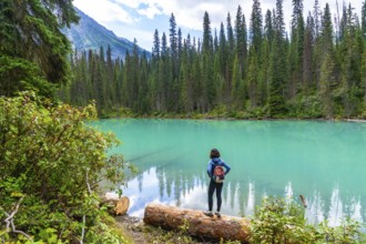 Hiker standing on a log, admiring the stunning turquoise waters of emerald lake, surrounded by lush