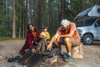 Family with little boy making campfire near their campervan during their vacation camping in the