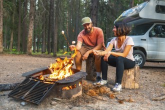 Tourists are roasting marshmallows over a campfire near their campervan in a campsite in banff