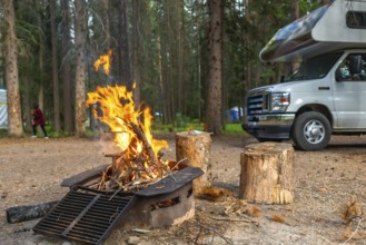 Warm fire glowing in a campsite fire pit beside a camper van in banff national park, alberta,
