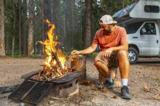 Tourist feeding campfire flames near camper van in banff national park, canadian rockies, alberta,