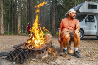 Camper enjoying warmth of campfire in banff national park, canadian rockies, with campervan parked