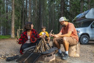 Family enjoying camping in the canadian rockies, preparing campfire next to their campervan in